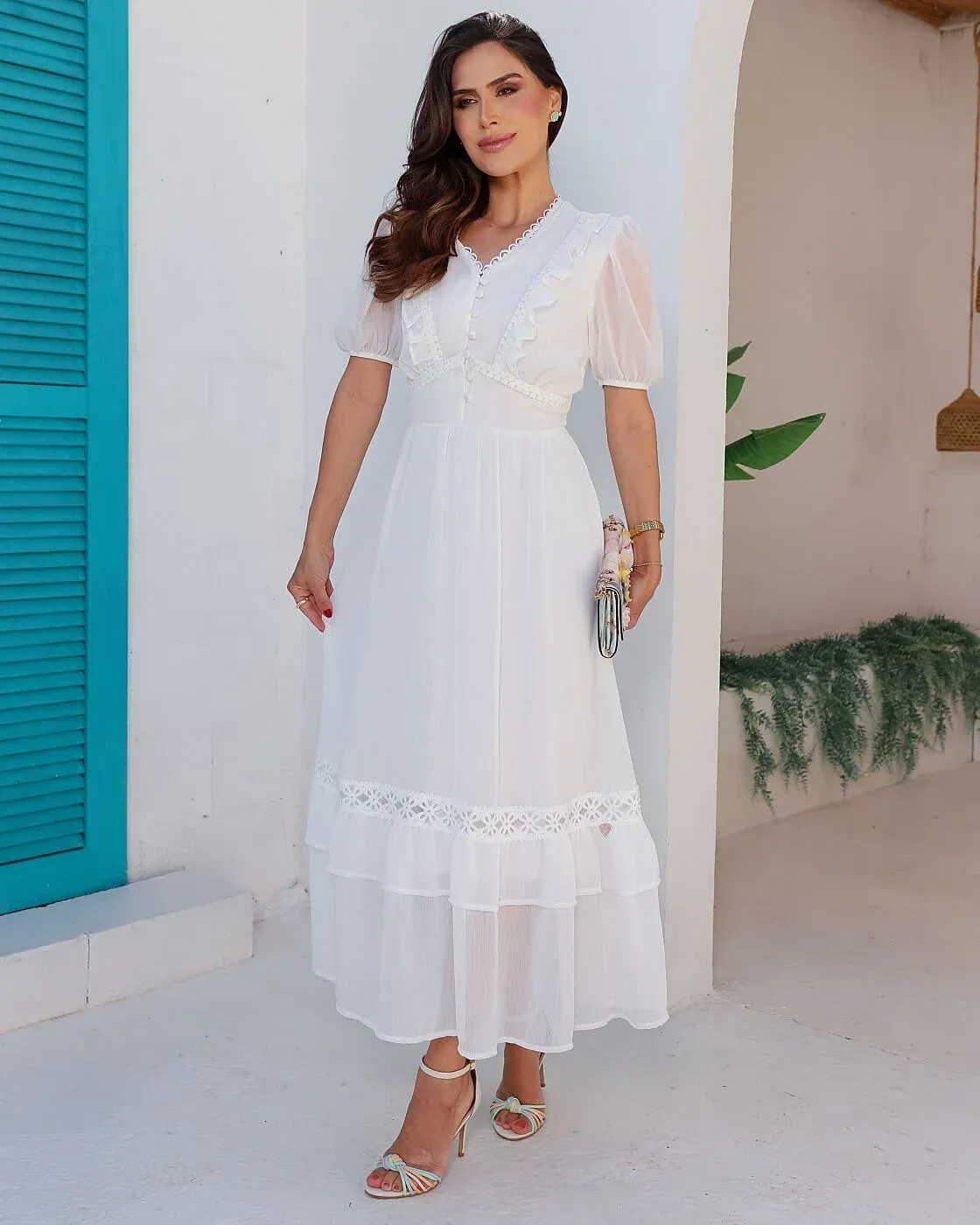 O Vestido Nicoly, em um clássico tom branco, possui decote em V com acabamento em renda, mangas curtas bufantes com leve transparência, botões encapados e cintura marcada. Sua saia longa e fluida apresenta renda guipir e babados em camadas, trazendo leveza e movimento.