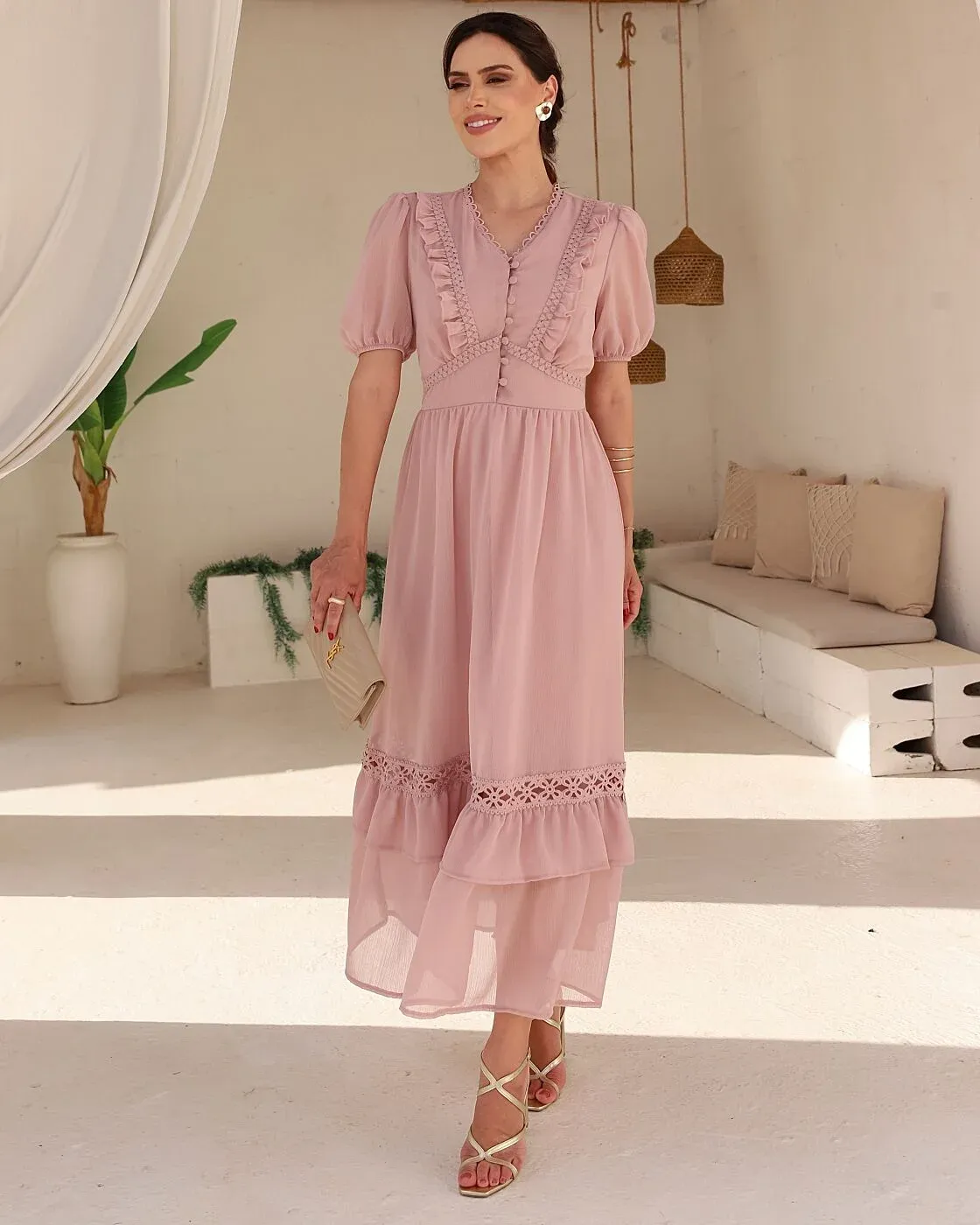 O Vestido Nicoly, em um delicado tom rosé, possui decote em V com acabamento em renda, mangas curtas bufantes e botões encapados no busto. Apresenta detalhes de babados e renda guipir que valorizam a região do colo e a cintura marcada. Sua saia longa e fluida possui delicados franzidos, aplicação de renda e babados em camadas na barra, proporcionando leveza e movimento. Uma peça romântica, feminina e sofisticada, perfeita para ocasiões especiais.